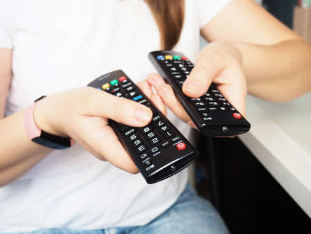 Hands holding the TV remote control, close-up at home.の写真素材