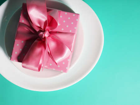 A gift box with a pink ribbon lies on the plates saucers on a mint-colored backgroundの写真素材