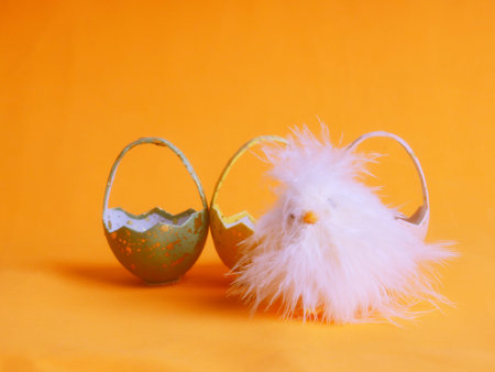 Small white chicken next to colored eggs for Easter on orange.