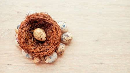 Quail eggs in a nest of branches lying on a wooden background, a postcard for Easterの写真素材