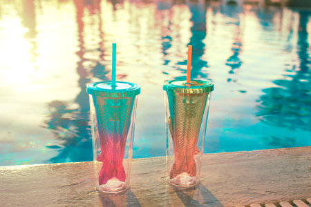beach holidays background with two cocktails In mermaid tail glass near swimming pool in luxurious...