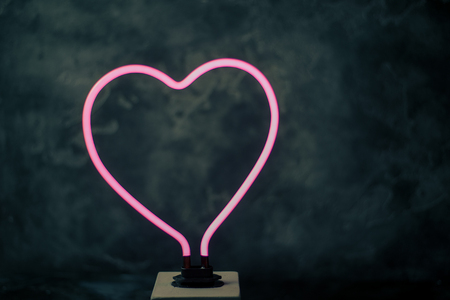glowing neon heart shape with black textured backの写真素材