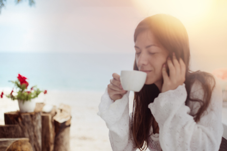 Blurred background with girl enjoy her aromatic coffee drink on a beach. White clear cup from a cafe.の写真素材