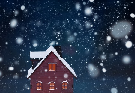 Miniature Christmas village scene with toy wooden house windows lit with yellow light with dark blue background, smoke out of chimney and snow falling. Greeting card concept.の写真素材