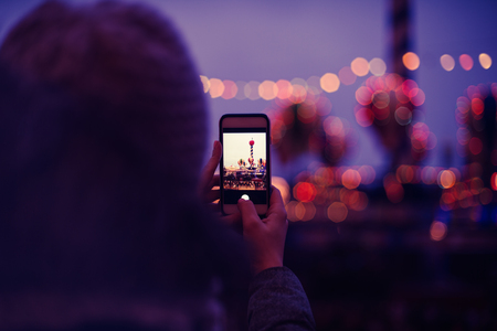 Woman Taking Pictures of European Christmas Market Scene on Smartphone. Girl Enjoying Winter Holiday Season, visiting Outdoors Christmas Market.の写真素材