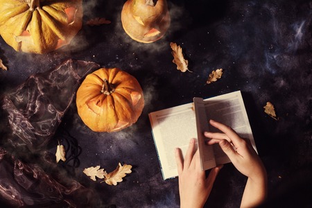 top view of woman reading book surrounded by halloween pumpkins with smoke and witch hatの写真素材