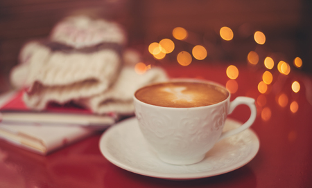 Cappuccino or latte coffee with heart shape on red table, books mittens and bokeh in backgroundの写真素材