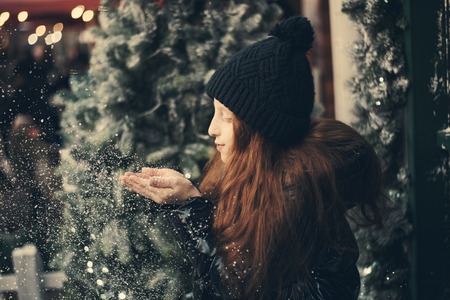Little girl blows snow from her hands on a snowflakes bokeh background.の写真素材