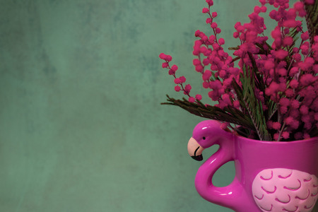 Pink mug or flower pot of flamingo shape with pink mimosa on a dark emerald green backgroundの写真素材