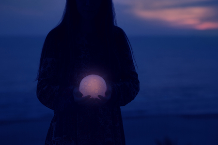 Beautiful attractive girl on a night beach with sand and stars holds the moon in her handsの写真素材