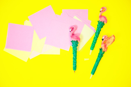 Desktop flatlay: pen with flamingo and pink paper lying vibrant yellow backgroundの写真素材