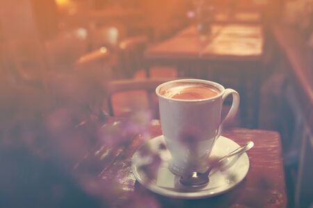 Close up white coffee latte cup on table near window with sun flareの写真素材