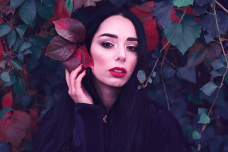 Young fashionable woman in a romantic autumn scenery with dark green red leavesの写真素材