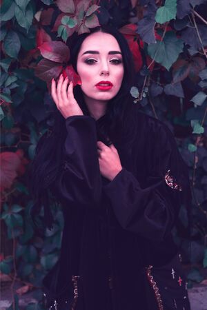 Young fashionable woman in a romantic autumn scenery with dark green red leavesの写真素材