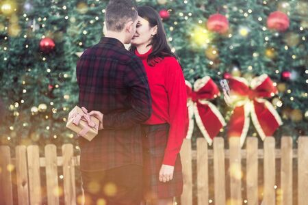 Winter couple holding gift against blurry christmas tree outdoorsの写真素材