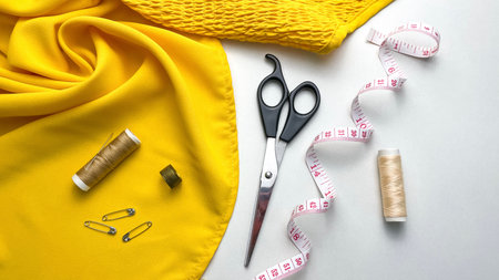 Sewing supplies are laid out on a white table and yellow fabric for working with textiles and handicrafts.の写真素材