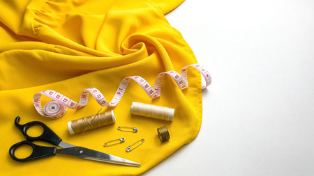 On the table are laid out tools for sewing on bright yellow fabric: scissors, thread, a measuring...