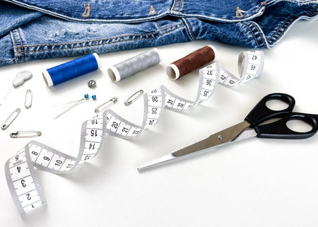 Sewing tools against a backdrop of blue jeans and a white table. Concept of sustainable fashion, clothing reuse, and home upcycling.の写真素材