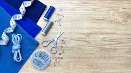 Sewing supplies next to clothing: measuring tape, thread, scissors, pins, and cord. Concept for home...