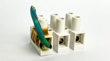 A close-up of a melted electrical terminal with a damaged insulated wire on a white background. This...