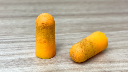 Two used foam earplugs with visible signs of contamination lie on a wooden surface. Concepts of...