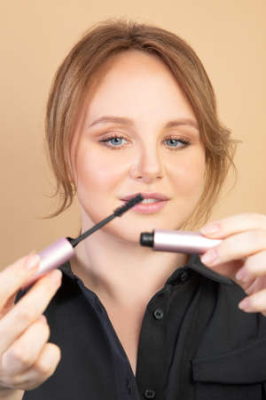 Girl paints mascara. beige backgroundの写真素材
