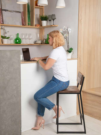 Blonde in a white T-shirt and jeans works behind a laptopの写真素材