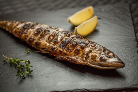 Delicious fish with vegetables and lemon on a black plate on the tableの写真素材