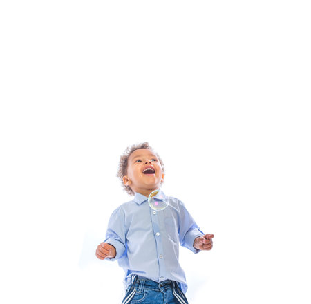 Portrait of a little dark-skinned toddler with curly hair looking up smiling seeing soap bubbles,...