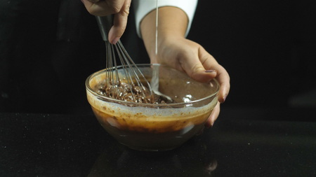 Making bakery chocolate cake. Whipping liquid chocolate with a whisk with the addition of milk in a thin stream on a black background.の写真素材