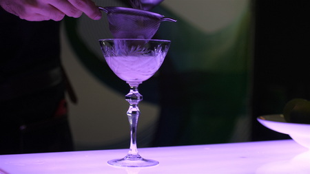 The process of making a cocktail, the barman in a beautiful glass on a long leg filters out the cocktail, a cocktail party, a contest of soft cocktails, a close-up video.の写真素材