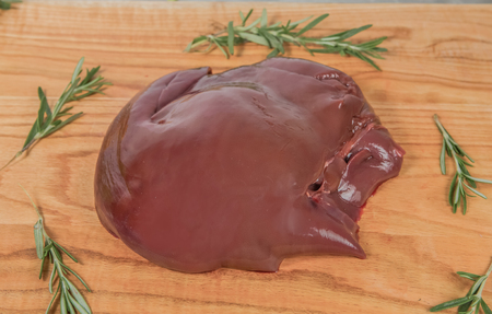 Fresh liver of a pig on a wooden cutting board with branches of rosemary. A close-up photo from aboveの写真素材