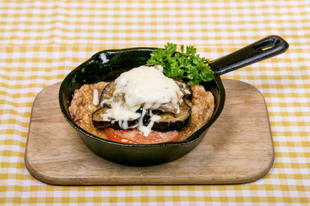 Fried eggplant with fried eggplant with sauce, decorated with a slice of tomato and a sprig of dill, the dish is served in a mini frying pan on a wooden board. Close-up photoの写真素材