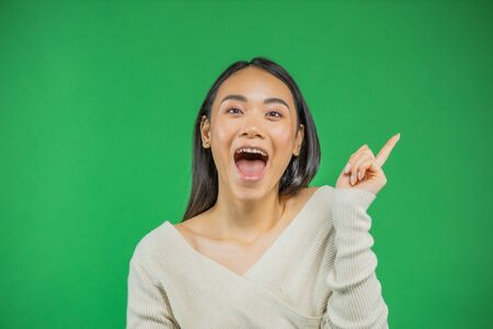 asian young woman pointing up isolated on green.の写真素材