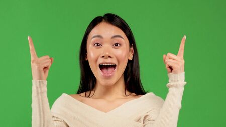 Beautiful Asian woman wearing white blouse over isolated background sign of success making positive hand gesture, pointing fingers smile and happy. Looking at the camera with a cheerful expression, the winnerの写真素材