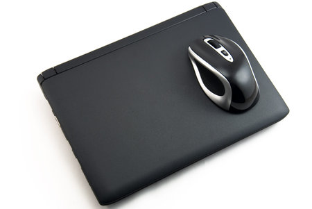 The wireless mouse lies on the closed laptop with a matte surface