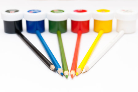 Six color pencils lie against jars with gouache