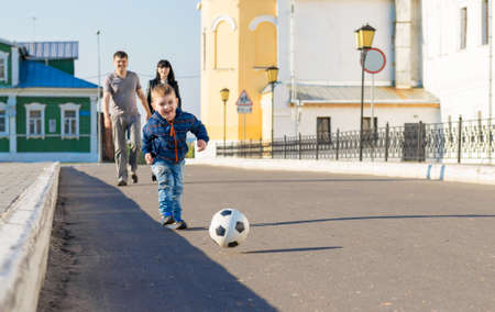 Cute little boy is walking in a park with his parents and carrying soccer ballの写真素材