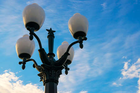 A pillar with four lamps. A lamppost against the sky with white clouds.の写真素材
