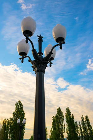A pillar with four lamps. A lamppost against the sky with white clouds.の写真素材