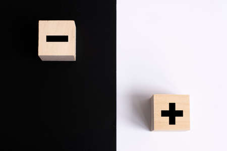 Symbols of black color plus and minus on wooden cubes on a white and black background. Abstractionの写真素材