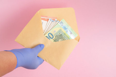 a hand in blue latex gloves holds an open envelope with different Euro banknotes. Bribe