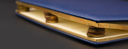 Blue diary with stacks of coins inside, isolated on black. Stash of moneyの写真素材