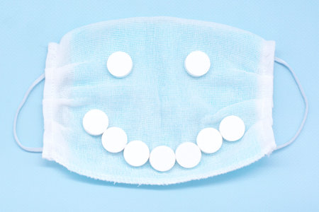 protective mask and smiling face from white tablets on a blue background. Coronavirus worldwide health threat.The concept of positivityの写真素材
