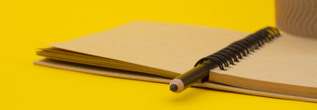 Minimalist template with copy space close up macro photo of wooden black pencil and craft diary on yellow backgroundの写真素材