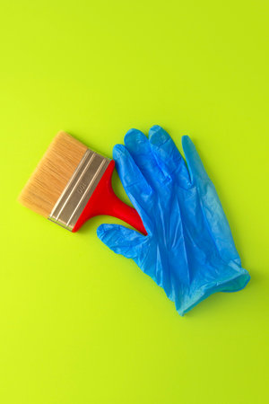 Female hand in blue gloves holds a red brush for painting on a green background. Repair concept. Flat layの写真素材