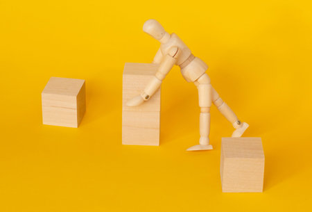 Mannequin with wooden cubes. A mannequin on a yellow background is holding wooden empty cubes.the...