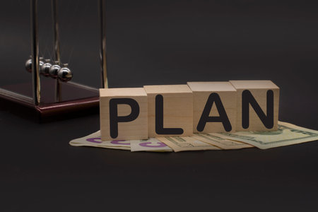 Word plan on wooden cubes, American dollars and Newton's cradle on office desk. Business conceptの写真素材