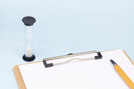 an hourglass and paper with a pen on a blue background. The concept of the transience of time.の写真素材