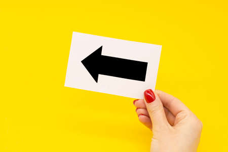 A woman's hand with a fashionable manicure holds an arrow pointer on a yellow background.の写真素材